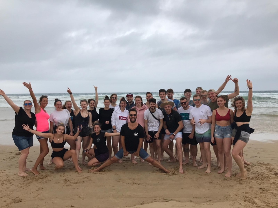 Large group of people posing on a sandy beach.