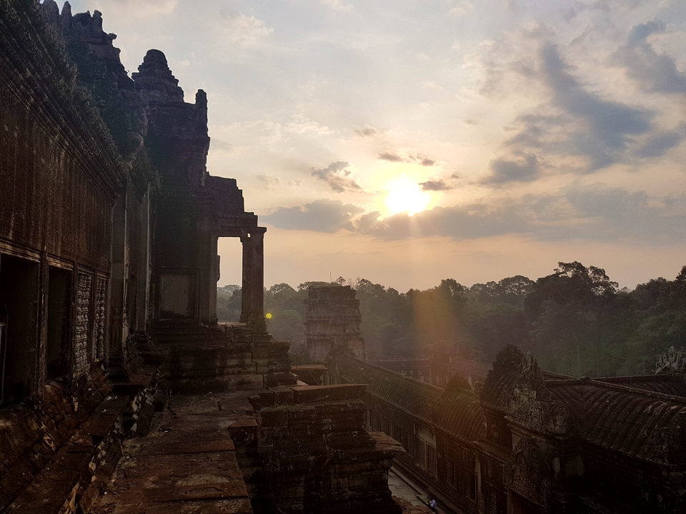 Sunset over ancient temple ruins with trees surrounding.