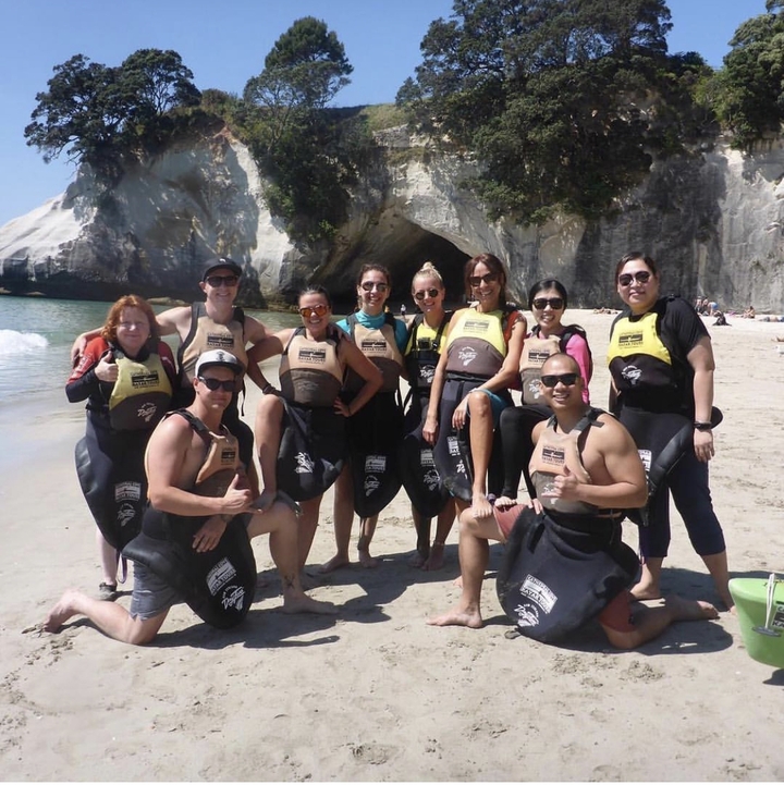 Group of people posing on a beach in wetsuits.