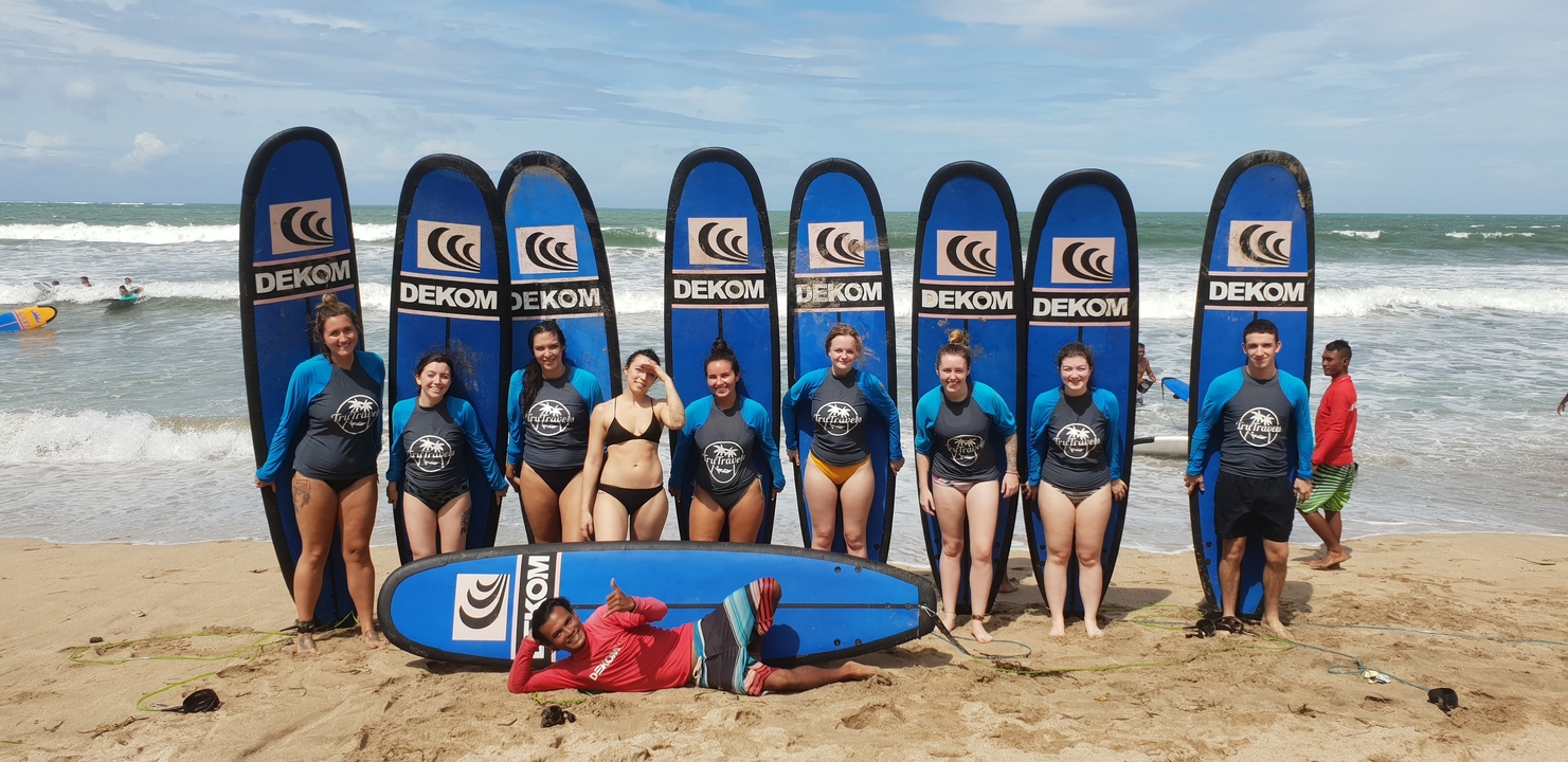 Group of people posing with surfboards on a beach.