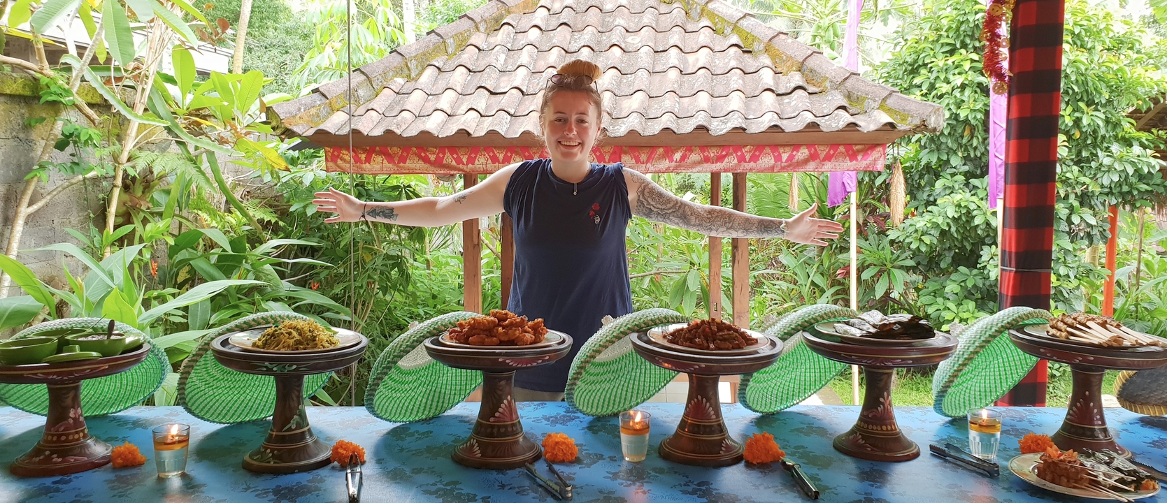 Person standing behind a table of dishes outdoors.