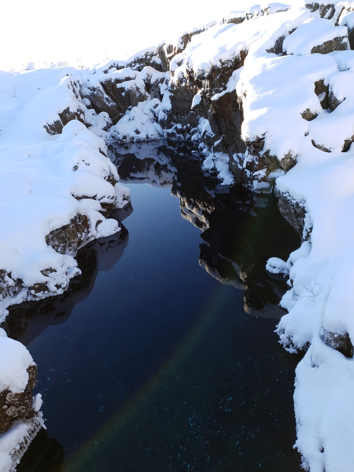 Reflections of snow-covered rocks in a calm, narrow stream.