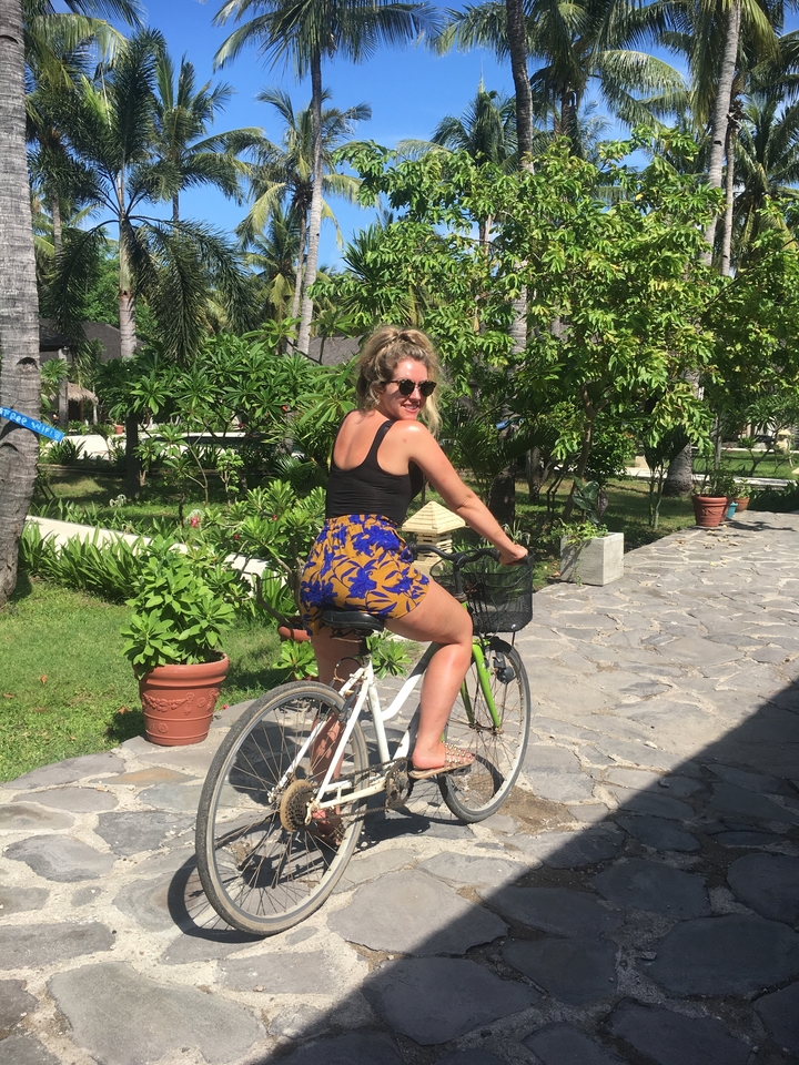 Woman riding a bicycle in a tropical garden setting.