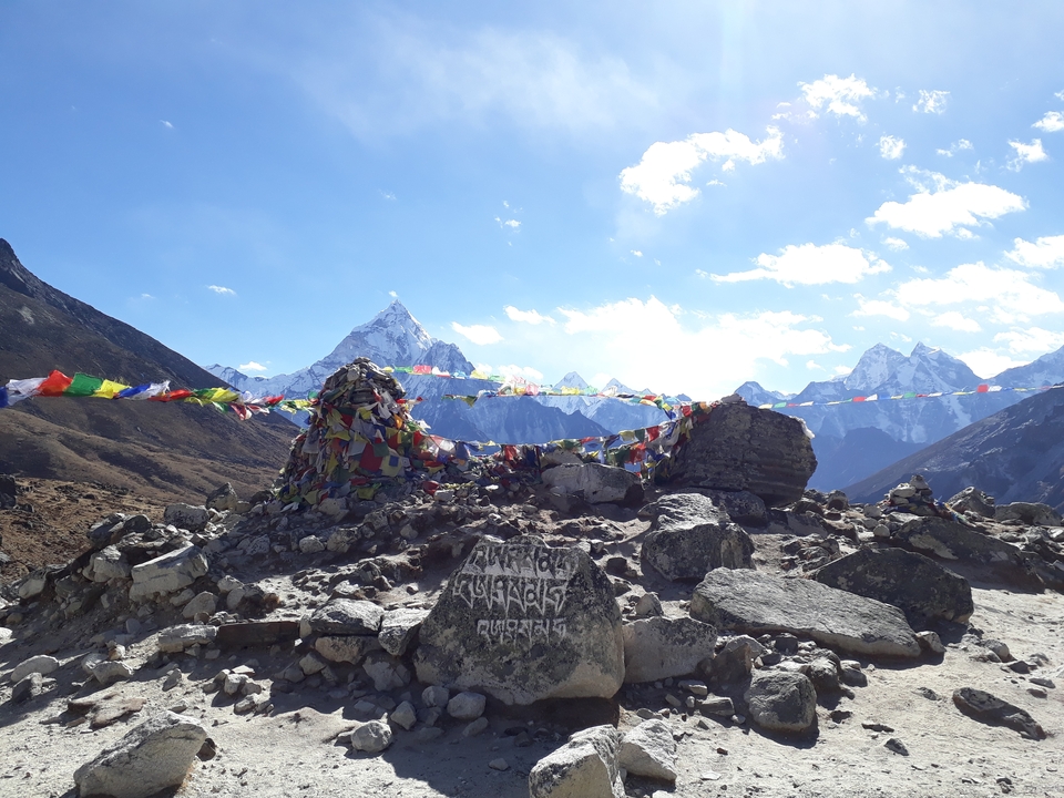 Cairns de pierres avec drapeaux de prière et montagnes enneigées en arrière-plan.