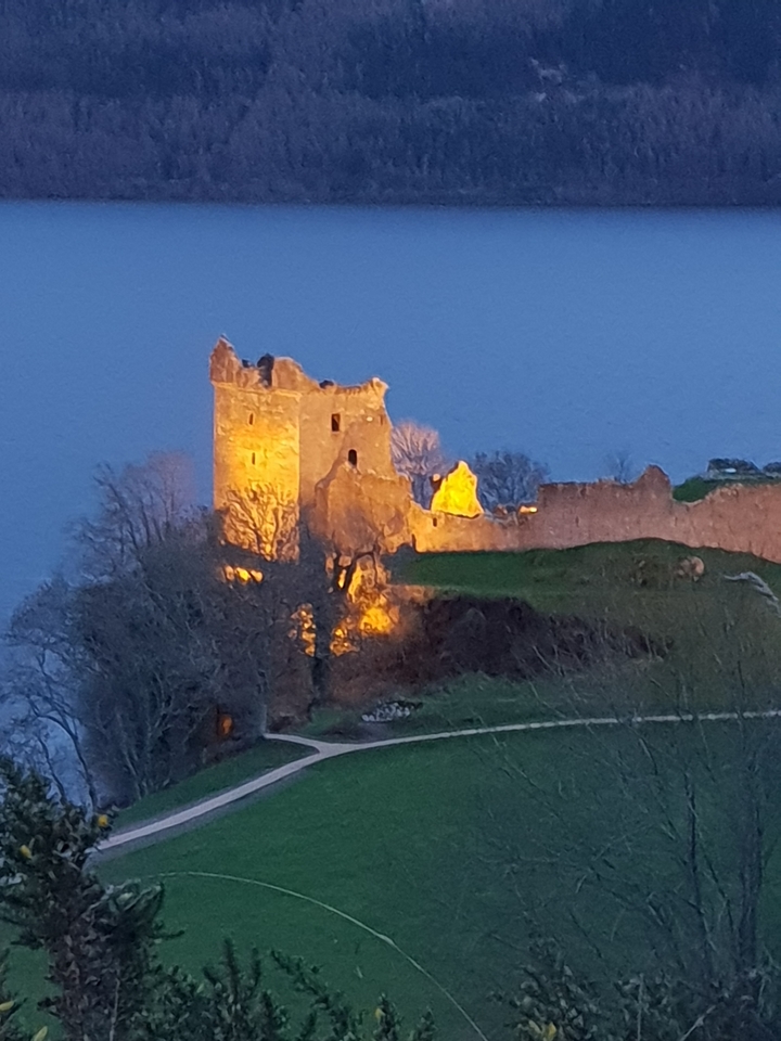 Illuminated castle ruins on a hill at dusk.