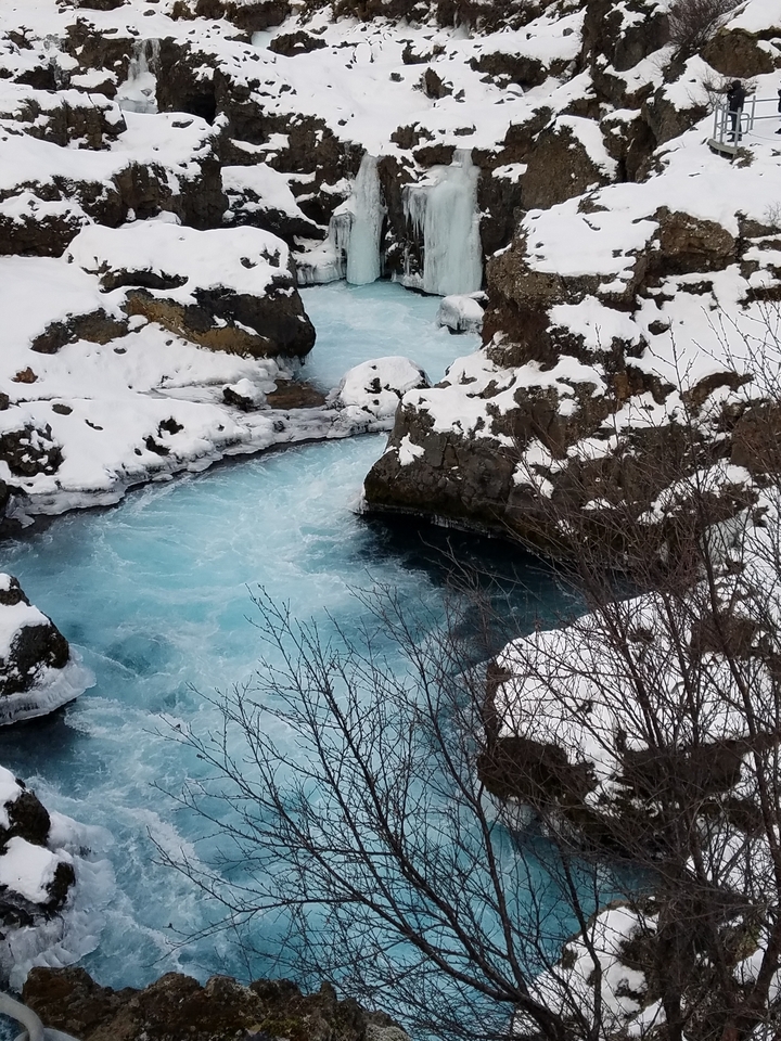 Frozen river with snow-covered banks and clear blue water.
