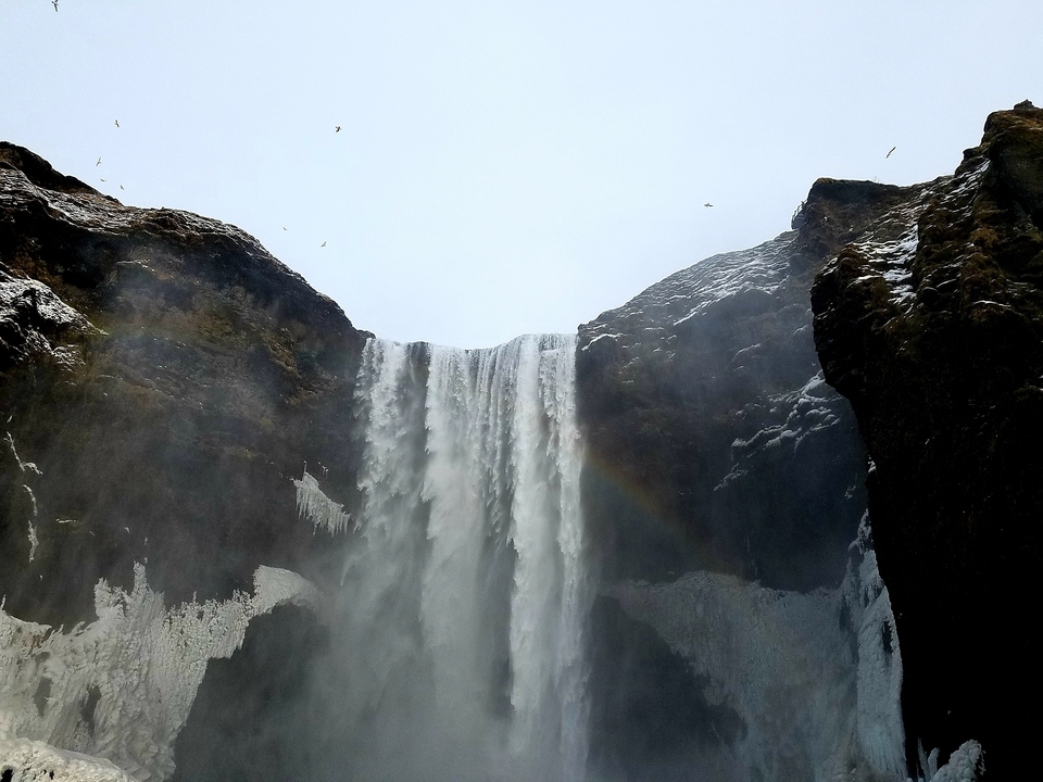 Waterfall cascading down a cliff with a rainbow on the right side.