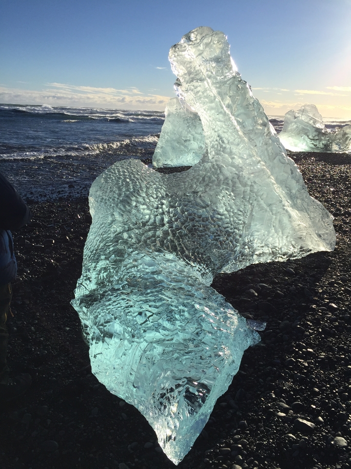 Crystal clear ice formations on a black pebble beach.