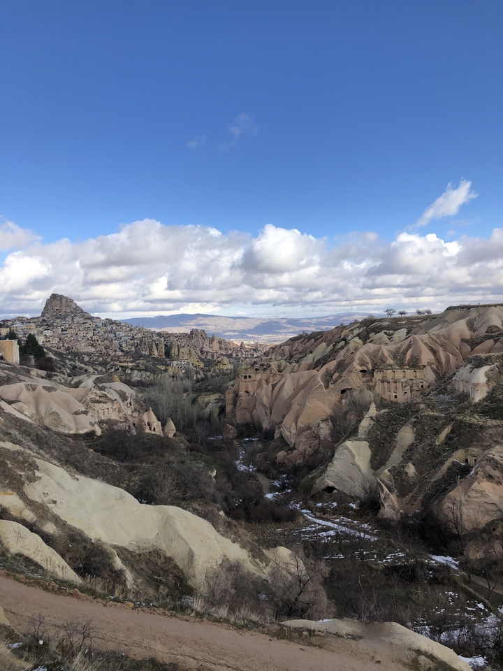 Rocky landscape with a village built into the hills, under a cloudy sky.