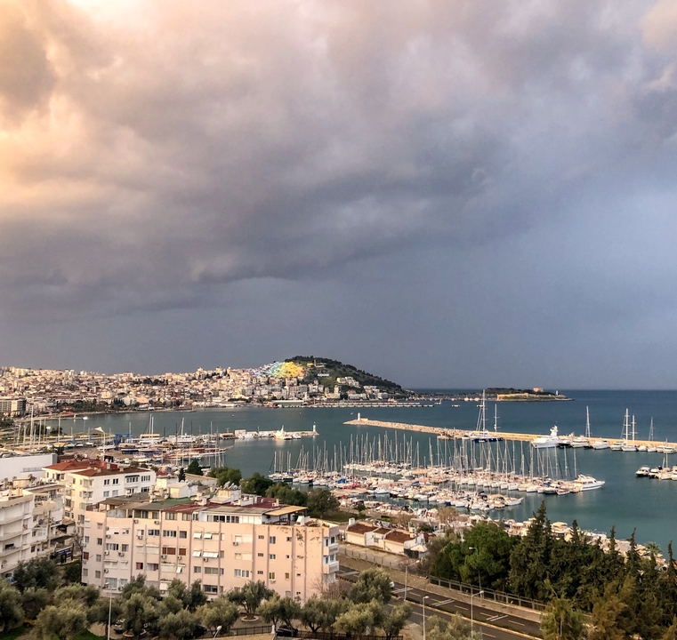 Harbor view with boats and a distant hill under a cloudy sky.