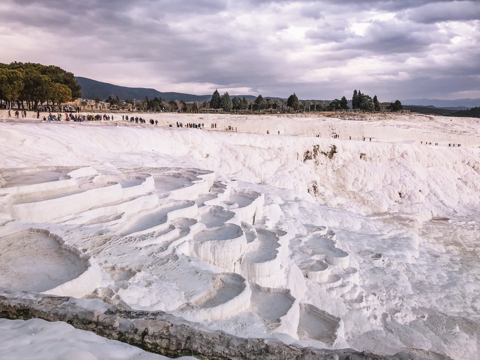 Terraced white travertine formations at Pamukkale with tourists in the distance.