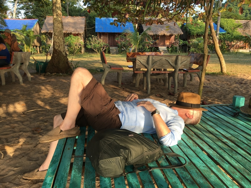 Personne se reposant à l'extérieur sur un banc coloré avec un chapeau couvrant son visage.