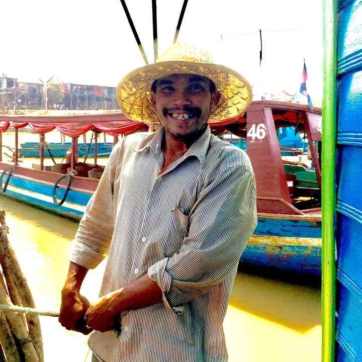 Homme souriant devant des bateaux à un quai.