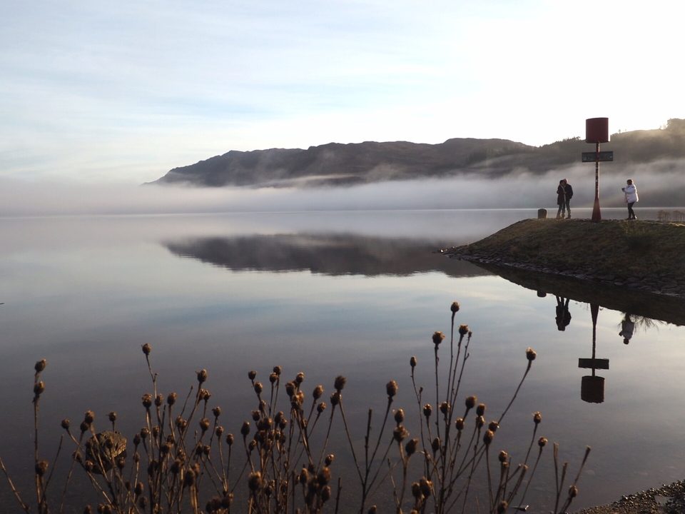 Calm water with reflections, people walking on a pier.