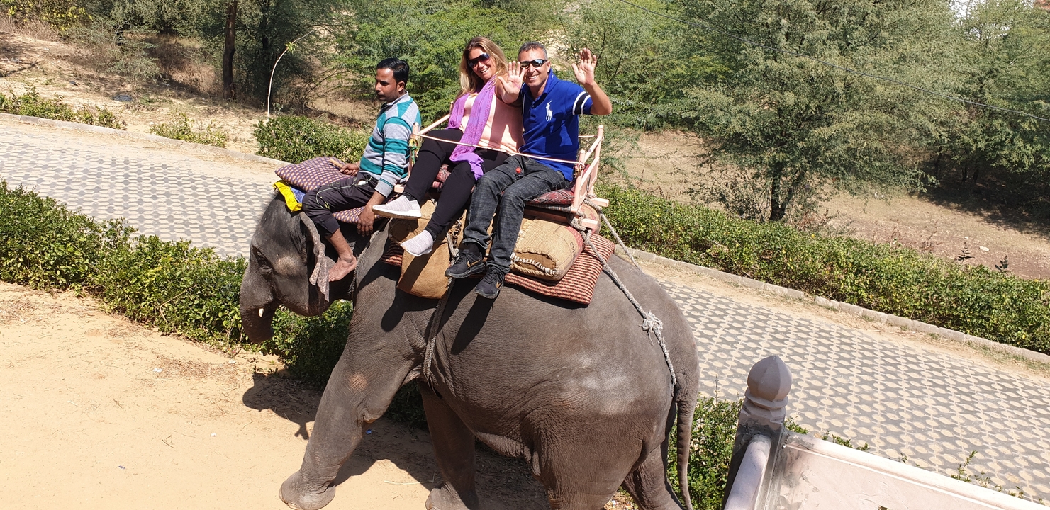 Three people riding an elephant during the day.