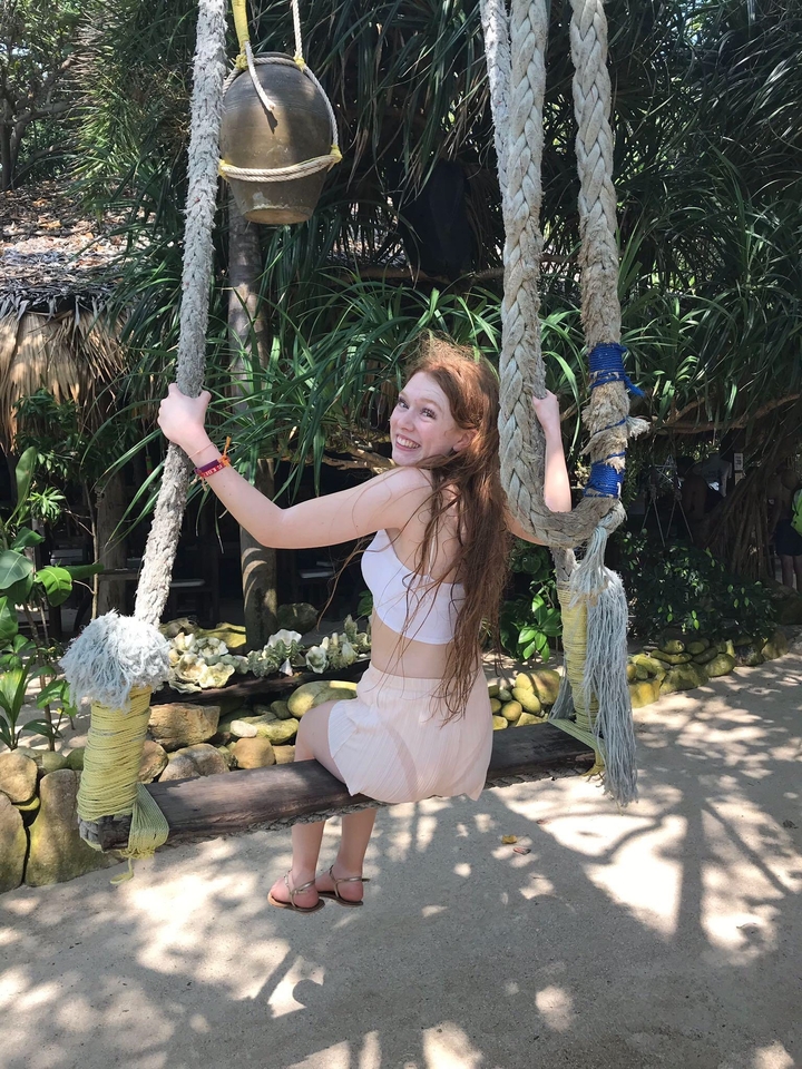 Woman standing on a swing by the beach, smiling.