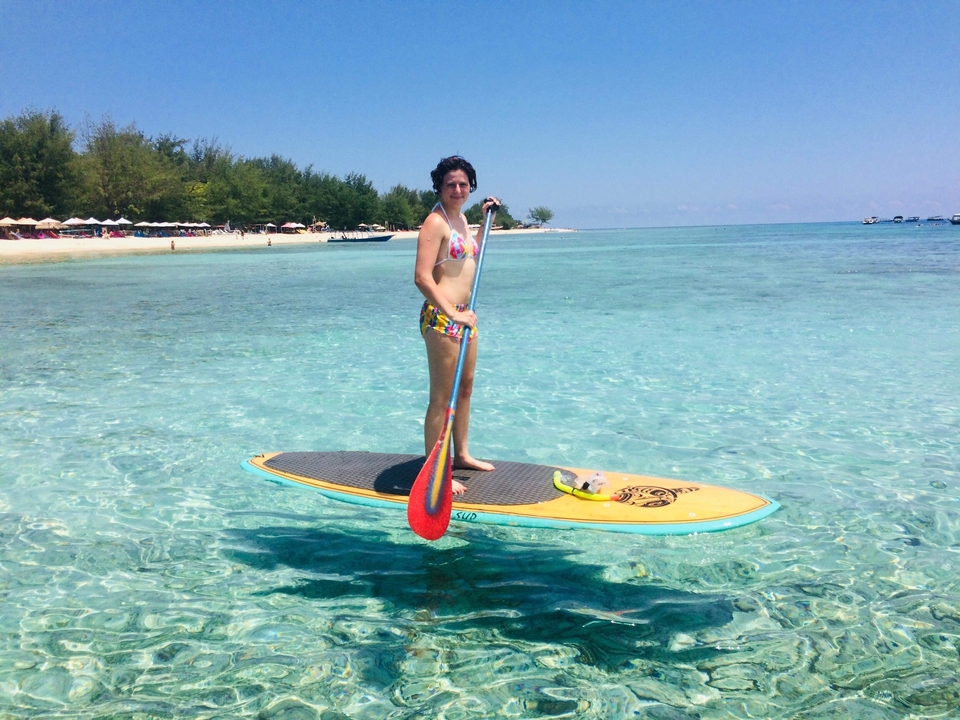 Person paddle boarding in clear ocean waters.