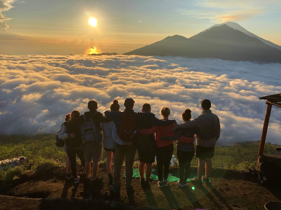 Group of people standing on a hill with a view of clouds and mountains at sunrise
