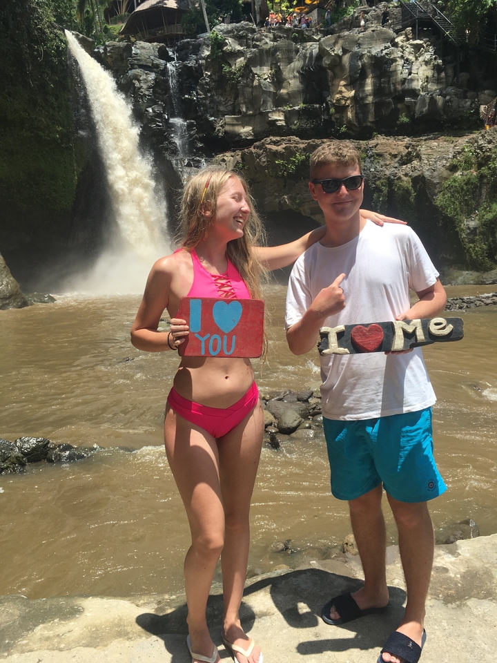 Two people near a waterfall holding humorous signs