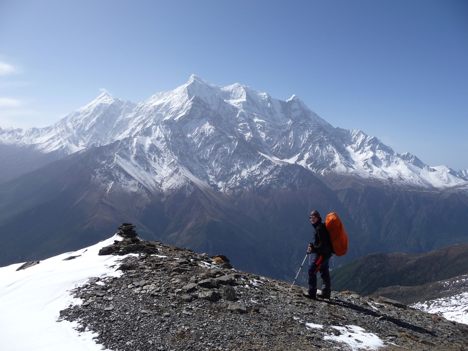 Hiker pauses on rocky ridge with vast snowy mountains filling the background.