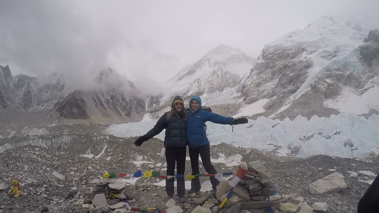 Deux personnes posant devant des montagnes enneigées avec des drapeaux de prière.