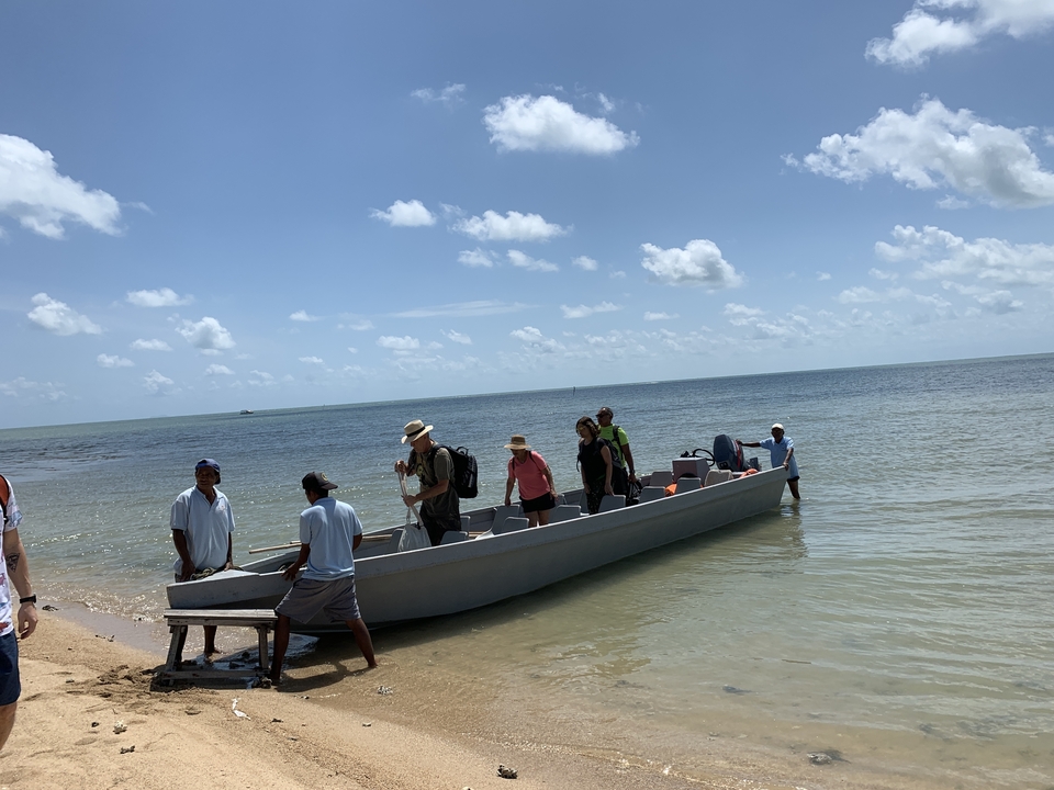 Des gens qui débarquent d'un bateau sur une plage de sable avec l'océan en arrière-plan.