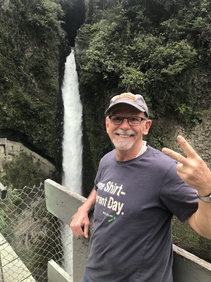 A man posing in front of a tall waterfall.