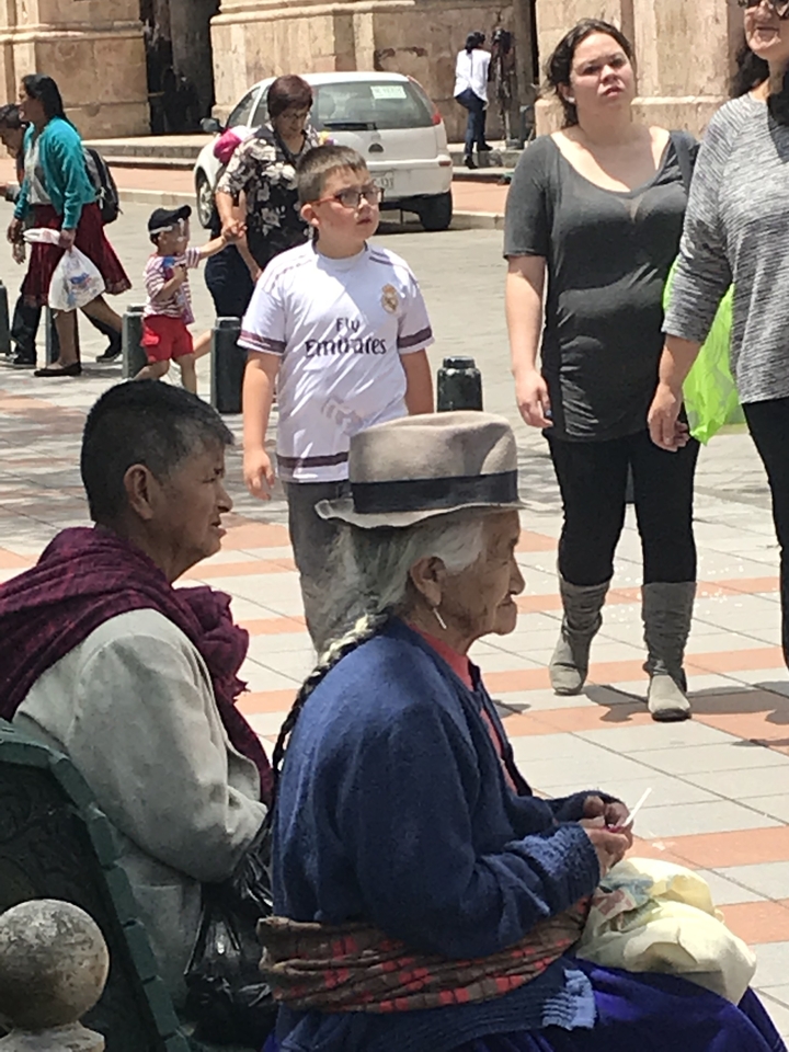 Two elderly people in traditional clothing sitting in an outdoor plaza.