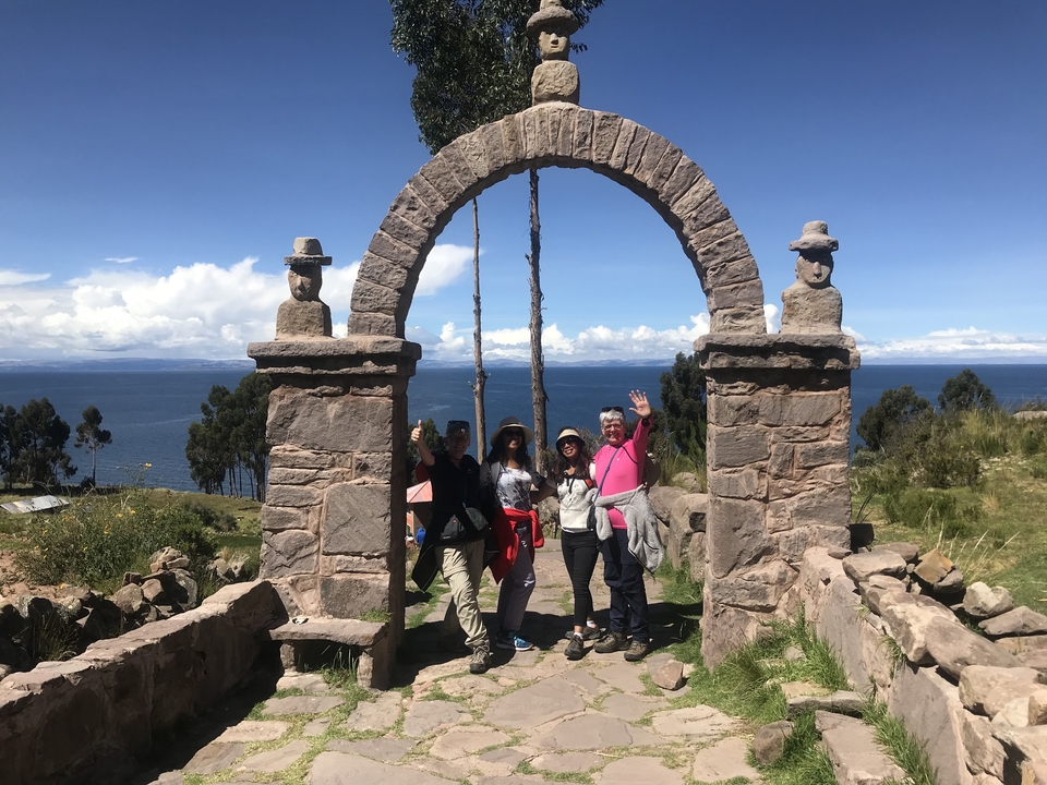 People standing under a stone arch with a view of a lake in the background.