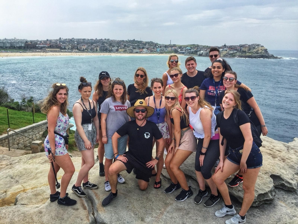 Group of people posing by the beach with a town in the background.