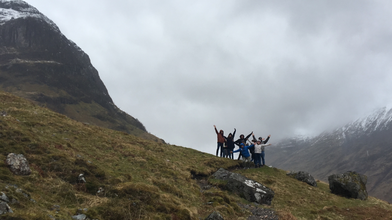 A group of people celebrating on a grassy hillside with mountains in the background.