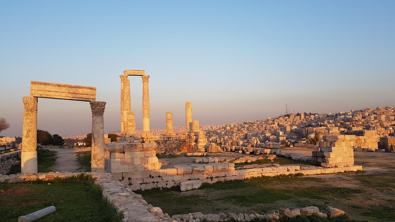 Ancient roman ruins with a sprawling cityscape in the background during golden hour.