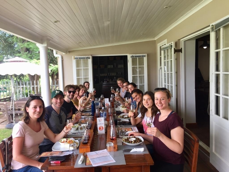 Group of people sitting around a long dining table outdoors.