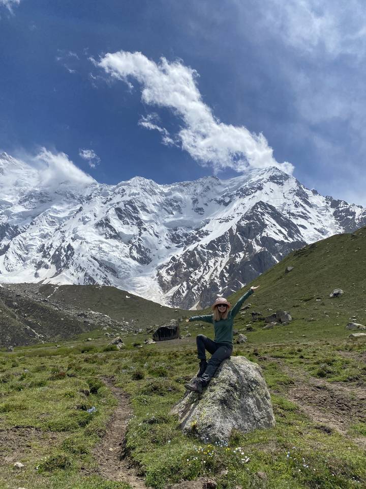 A person posing on a grassy hill with a snowy mountain view.