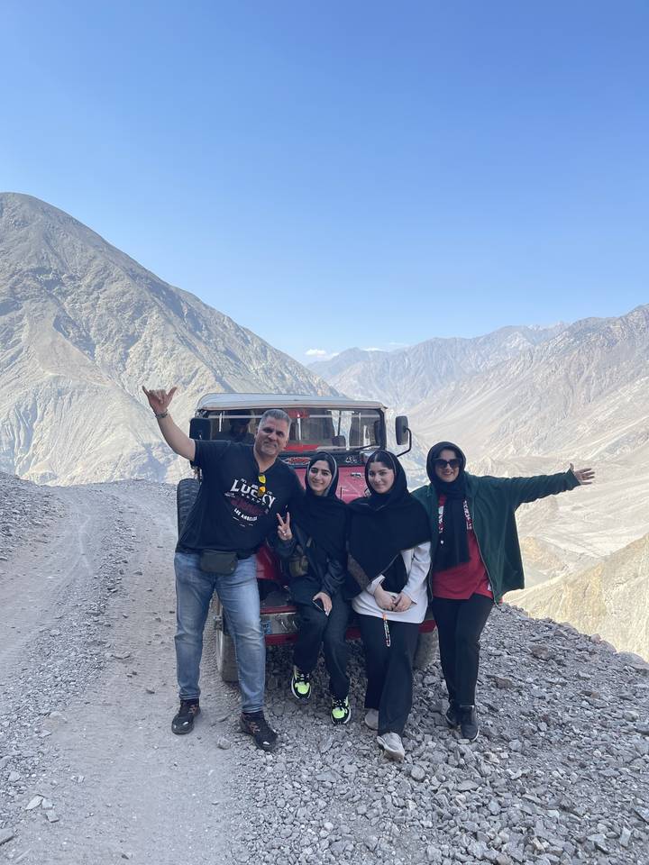 Group of people posing by a vehicle with mountains in the background.