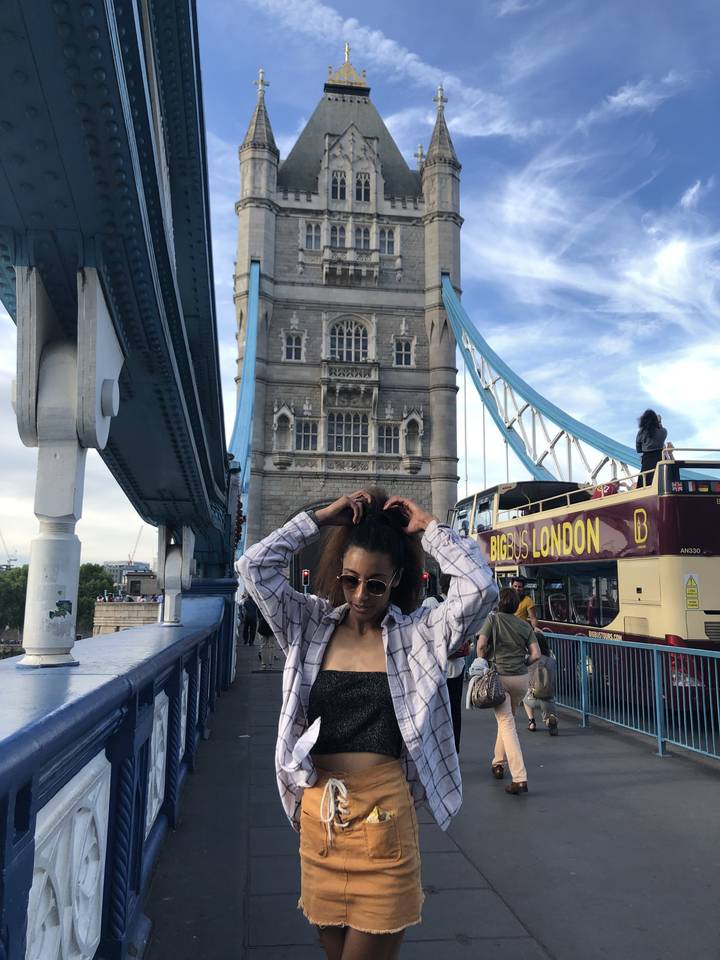 Woman posing on a bridge with a large tower in the background.