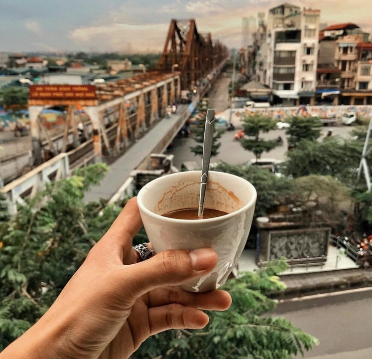 Hand holding a cup of Vietnamese coffee overlooking a busy street and bridge.