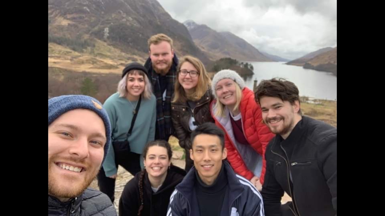 A group of friends with a scenic mountain and lake in the background.