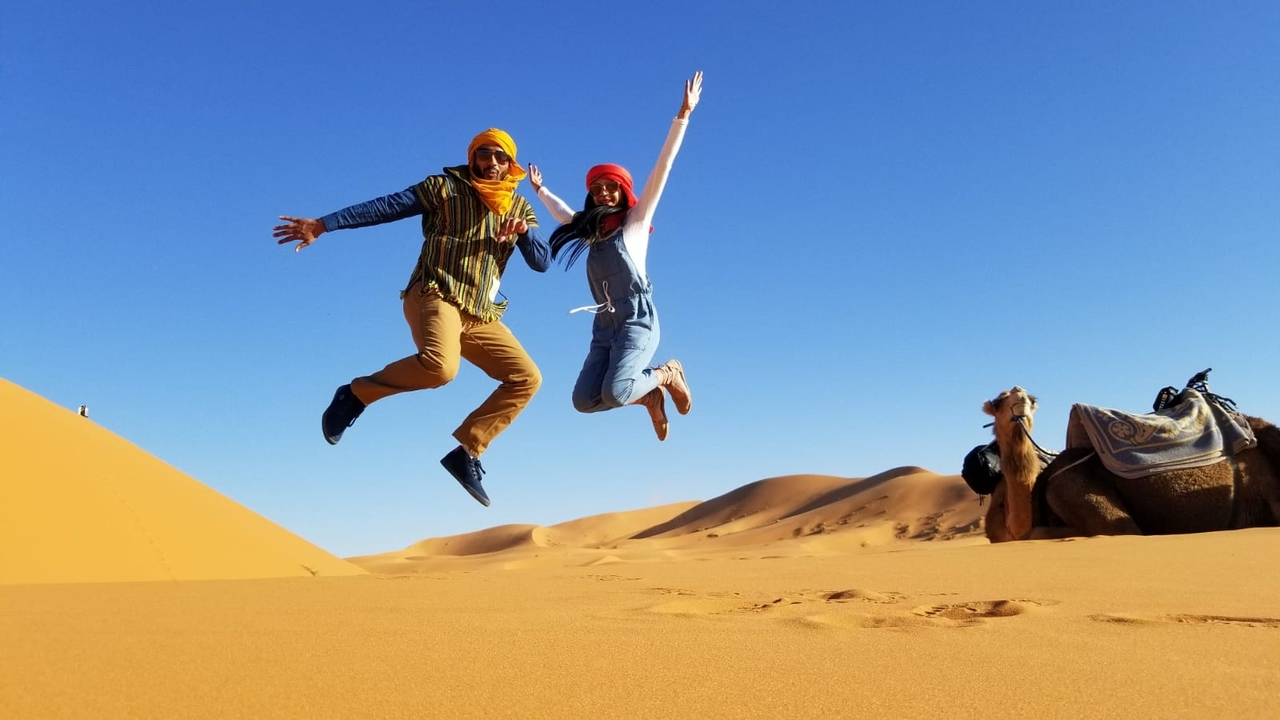 Two people jumping in the desert with a camel.