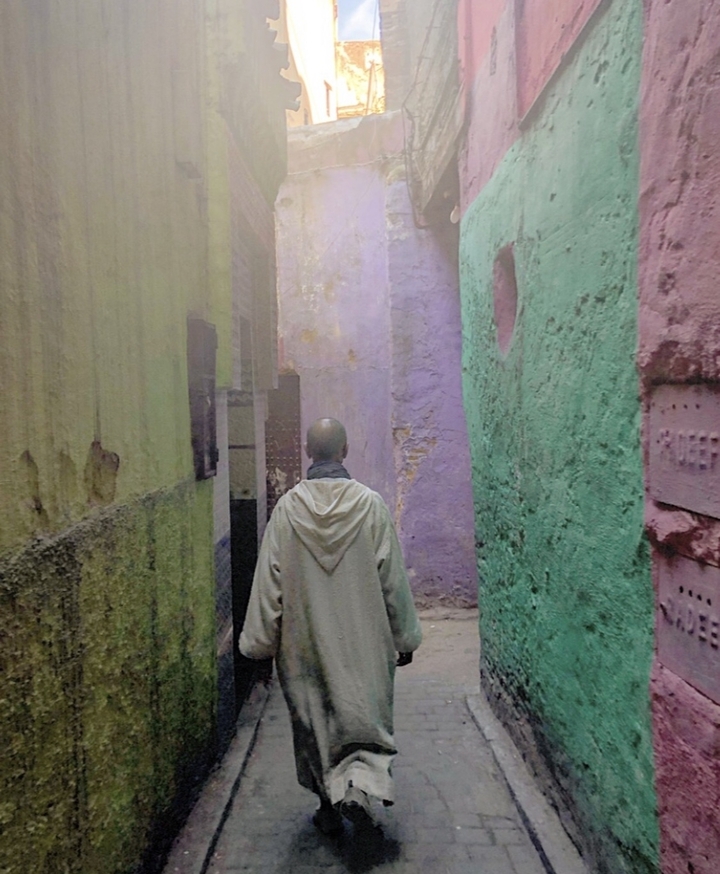 A person walking through a narrow alleyway with colorful walls.