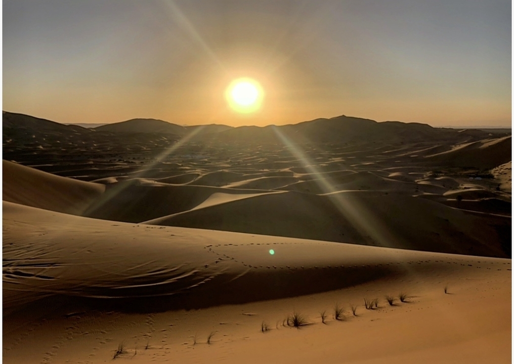A desert landscape with the sun setting over the dunes.