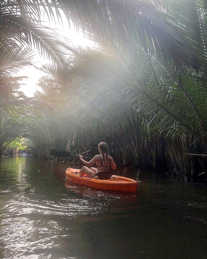 Person kayaking through a canal lined with trees.