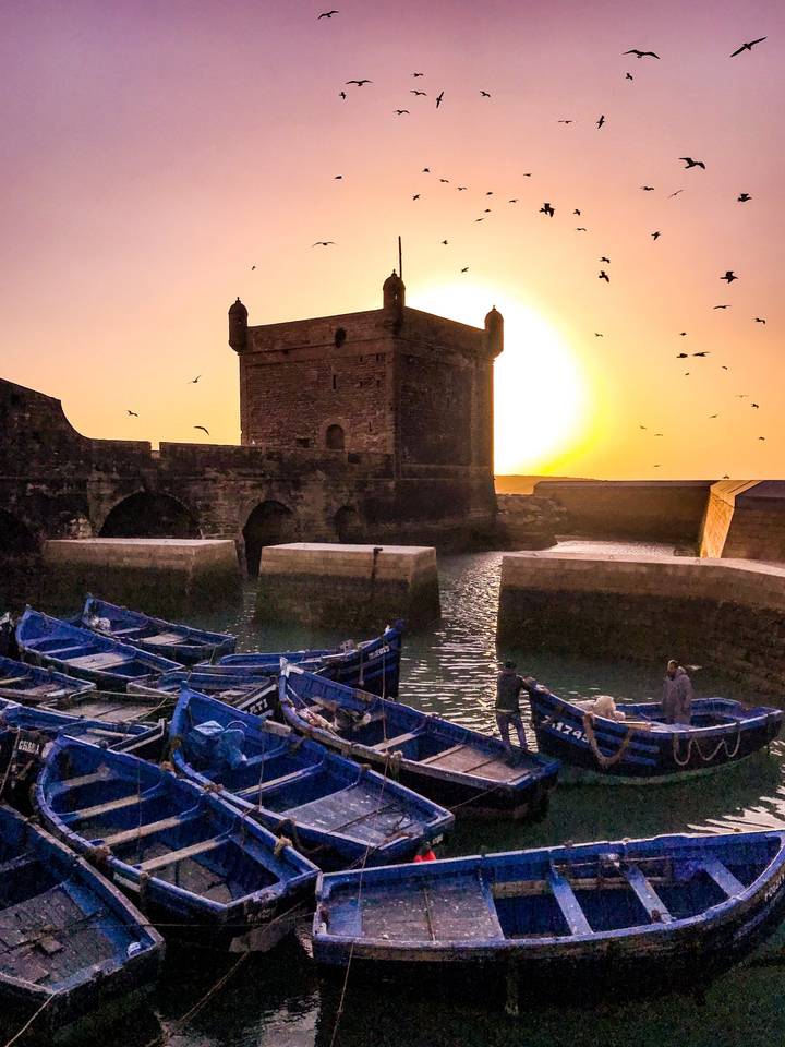 Sunset over a fortress with boats in the foreground.