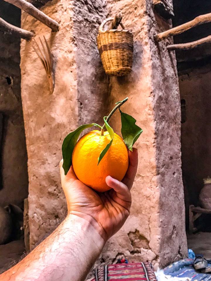 A hand holding a fresh orange with leaves.