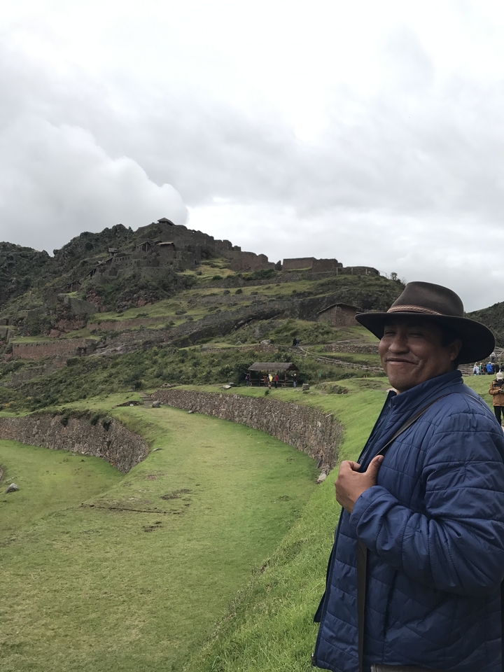 Personne portant un chapeau, debout près de ruines antiques sur une colline.
