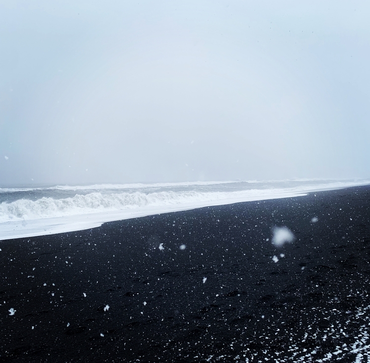 Black sand beach with waves and falling snow.