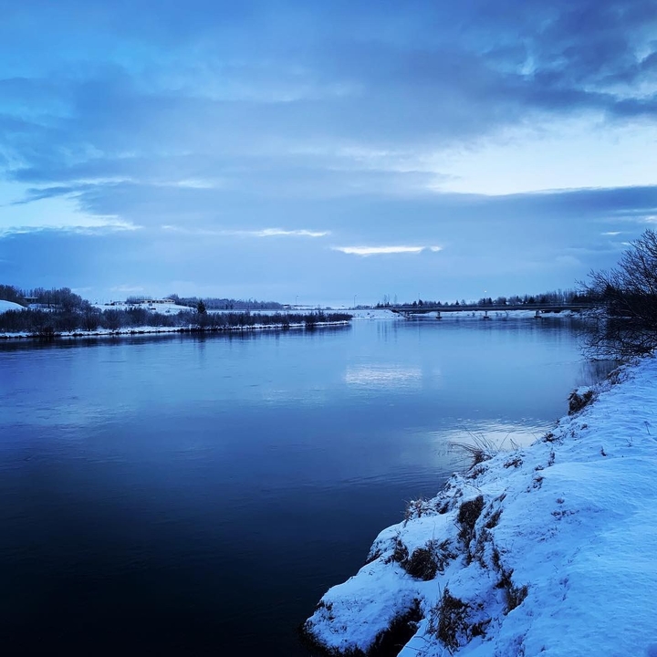 Tranquil river with snow-covered banks during twilight.