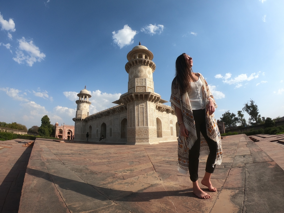 Femme souriante devant un mausolée blanc avec des minarets.