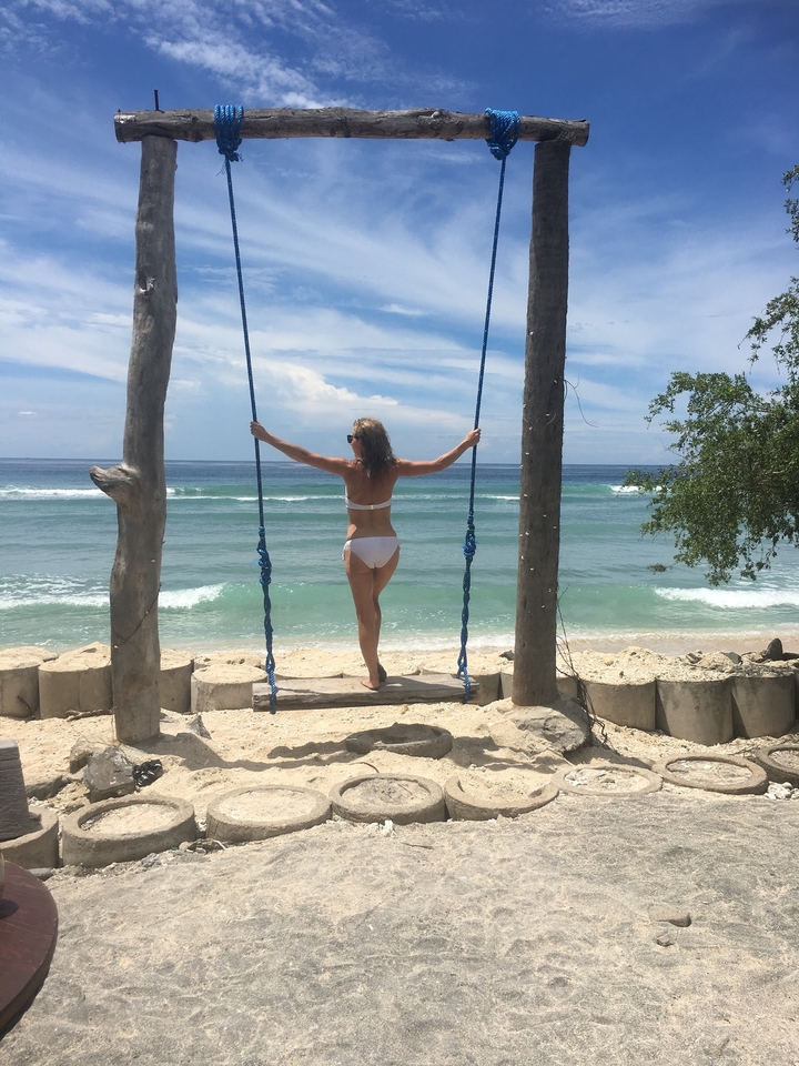 Woman on a beach swing overlooking the ocean.