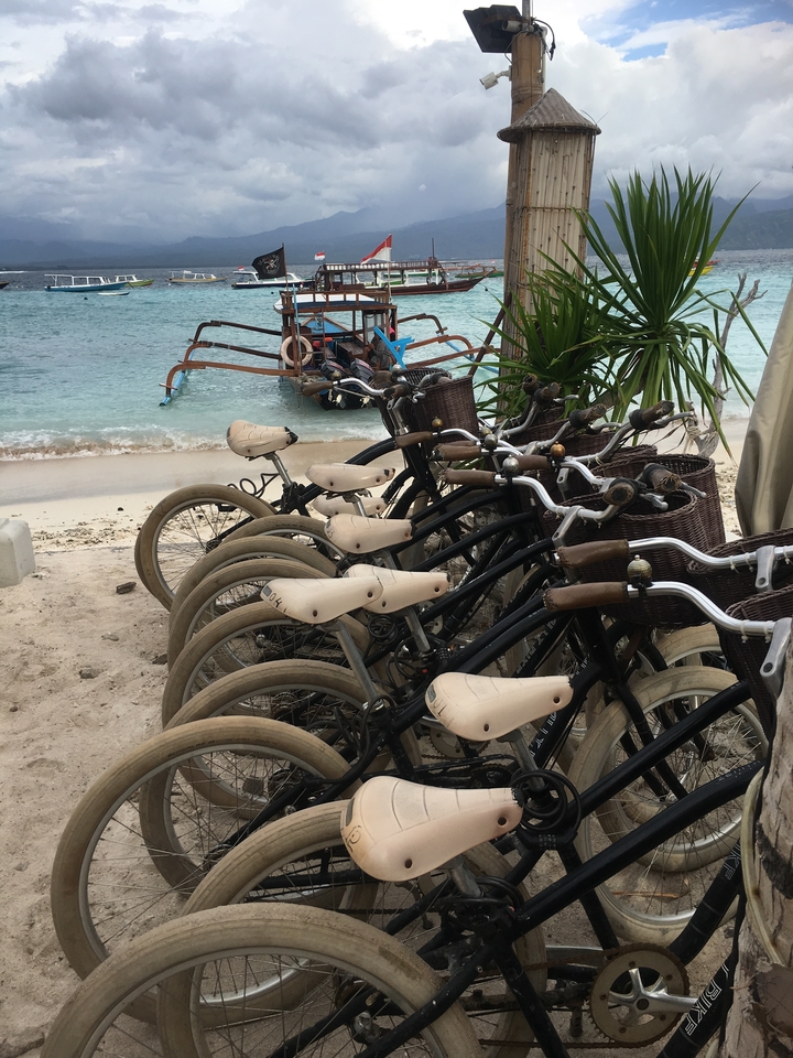 Row of bicycles parked on a beach with a boat in the background.